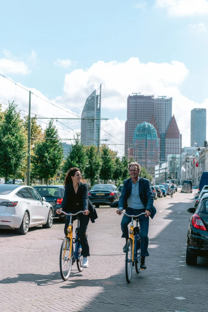 PBLQ- twee werknemers fietsen door Den Haag op een gele fiets